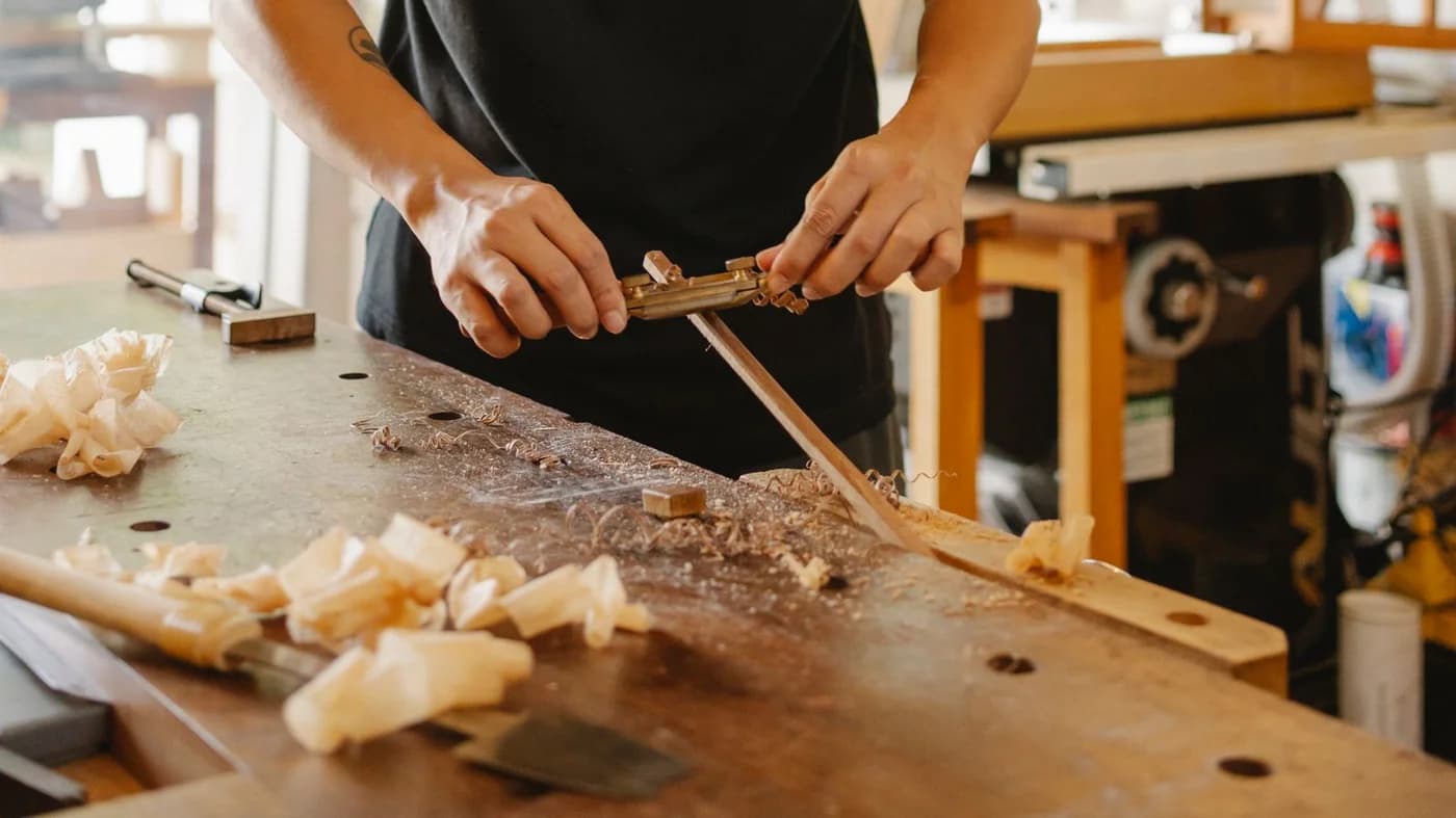 Craftsperson shaping a wooden piece with a hand tool